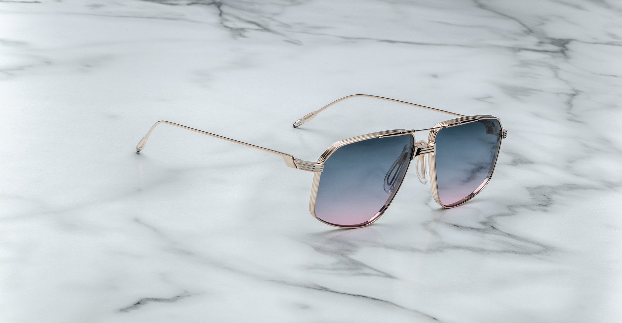 Jacques Marie Mage Jagger gold-framed oversized aviator sunglasses with gradient blue-pink lenses by Jacques Marie Mage, elegantly displayed on a white marble surface.