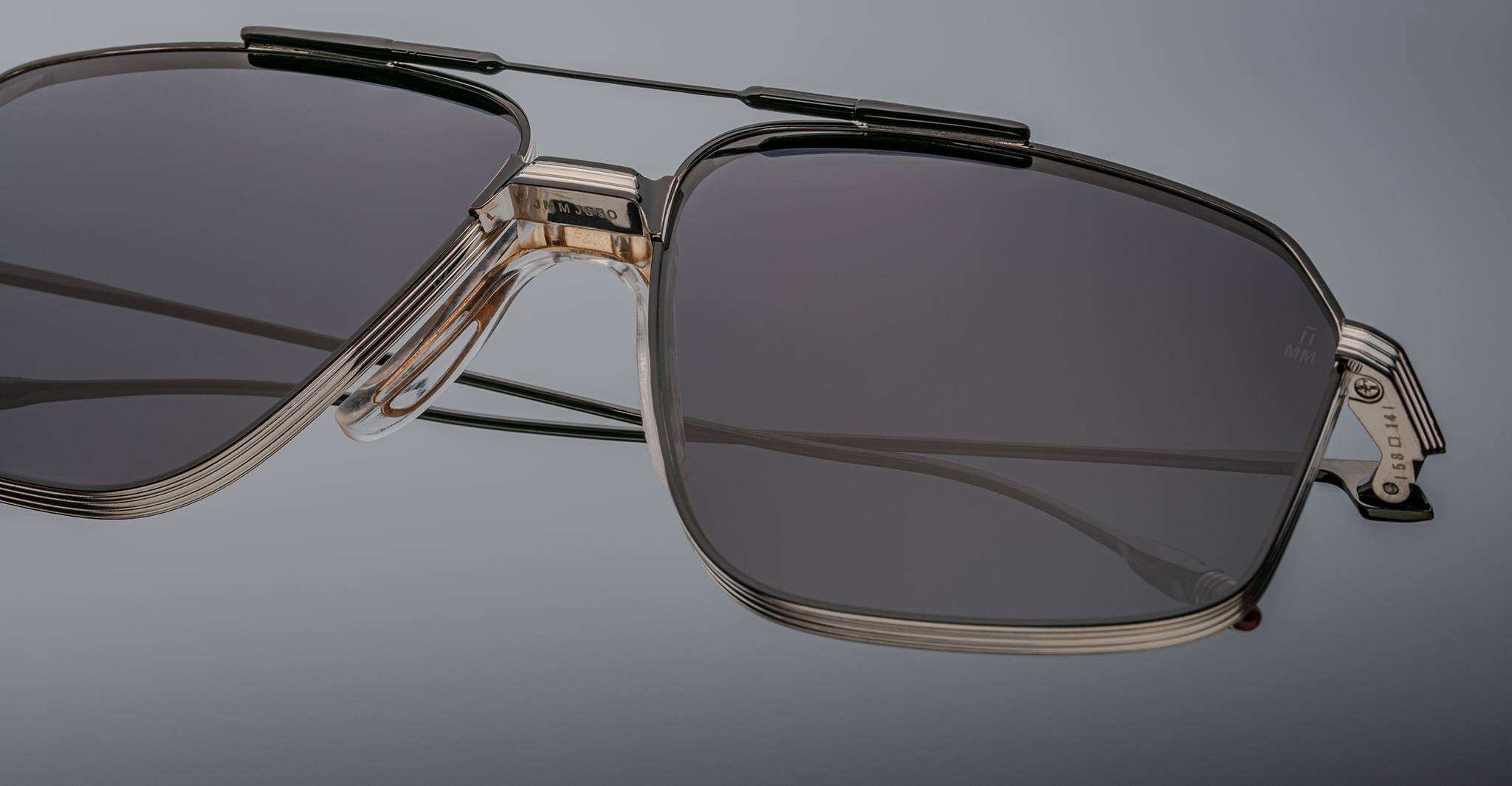 Close-up of Jacques Marie Mage Jagger rectangular sunglasses by Jacques Marie Mage, featuring dark lenses and metallic beta titanium frames against a plain background.