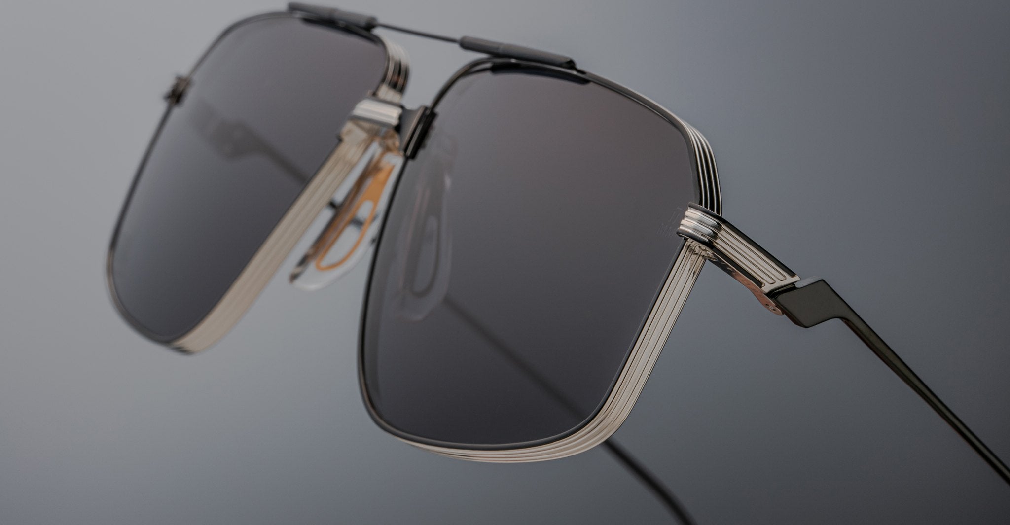 Close-up of Jacques Marie Mage Jagger sunglasses by Jacques Marie Mage, showcasing oversized aviator design with dark rectangular lenses and sleek beta titanium metallic frames against a neutral background.