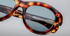 Close-up of Jacques Marie Mage Jennie sunglasses, tortoiseshell frame, blue lenses, silver accent at the hinge.