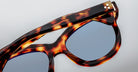 Close-up of Jacques Marie Mage Jennie sunglasses with blue lenses, detailed frame, and visible durable hinge.