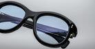 Close-up of Jacques Marie Mage Jennie sunglasses in black with blue-tinted lenses, UV protection details visible inside the temple.