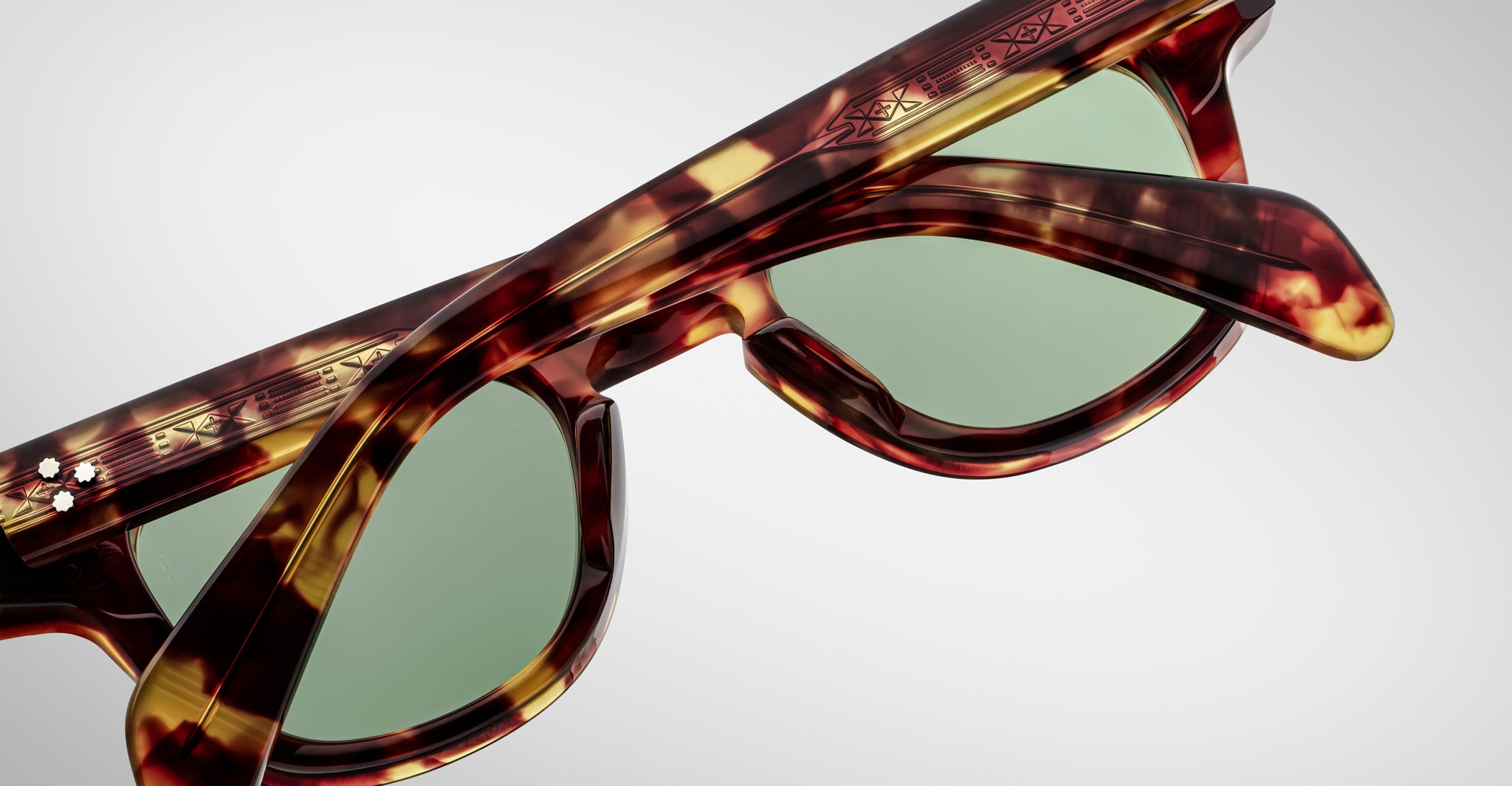 Close-up image of Jacques Marie Mage Julien tortoiseshell sunglasses with green-tinted lenses on a white background. Patterned arms and frame details are clearly visible.