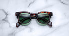 Jacques Marie Mage Julien in Havana 5 rectangular sunglass in brown tortoiseshell acetate with warm amber undertones, featuring a keyhole bridge, signature arrowhead front pins, and exposed metal core detailing within the temples, fitted with green-tinted lenses.
