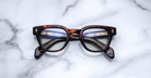 Jacques Marie Mage Julien in Havana 5 rectangular optical frame in rich brown tortoiseshell acetate with subtle amber highlights, featuring a keyhole bridge, signature arrowhead front pins, and exposed metal core detailing within the temples, shown with clear lenses.