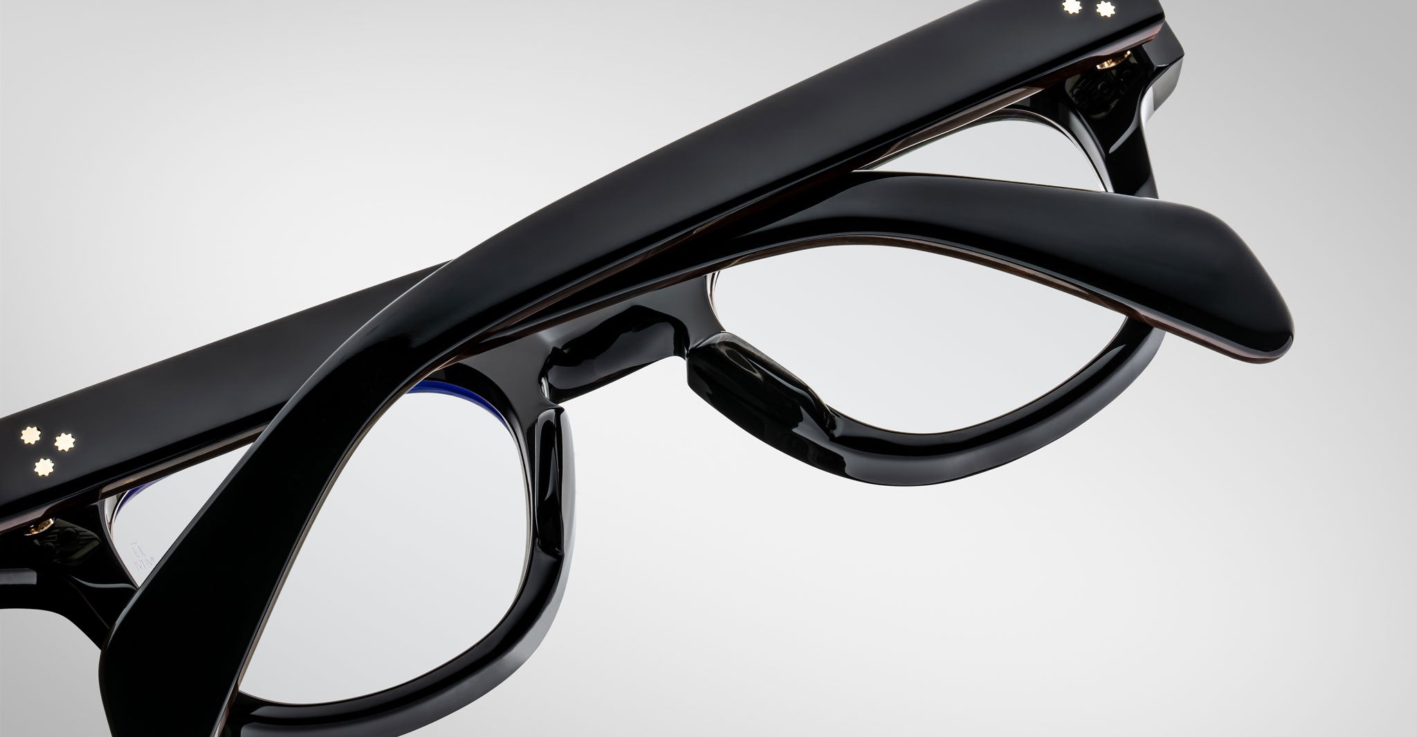 Close-up of Jacques Marie Mage Julien black eyeglasses with thick frames and temples, arms crossed over each other, set against a plain light gray background.