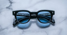 Jacques Marie Mage Julien in Titan rectangular frame in black acetate with cool blue undertones, featuring a keyhole bridge, signature arrowhead front pins, and exposed metal core detailing within the temples, fitted with blue-tinted lenses.