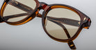 Close-up of Jacques Marie Mage Kay sunglasses in Teak brown with yellow-tinted lenses, highlighting fine craftsmanship and engraved inner arms, set against a neutral background.