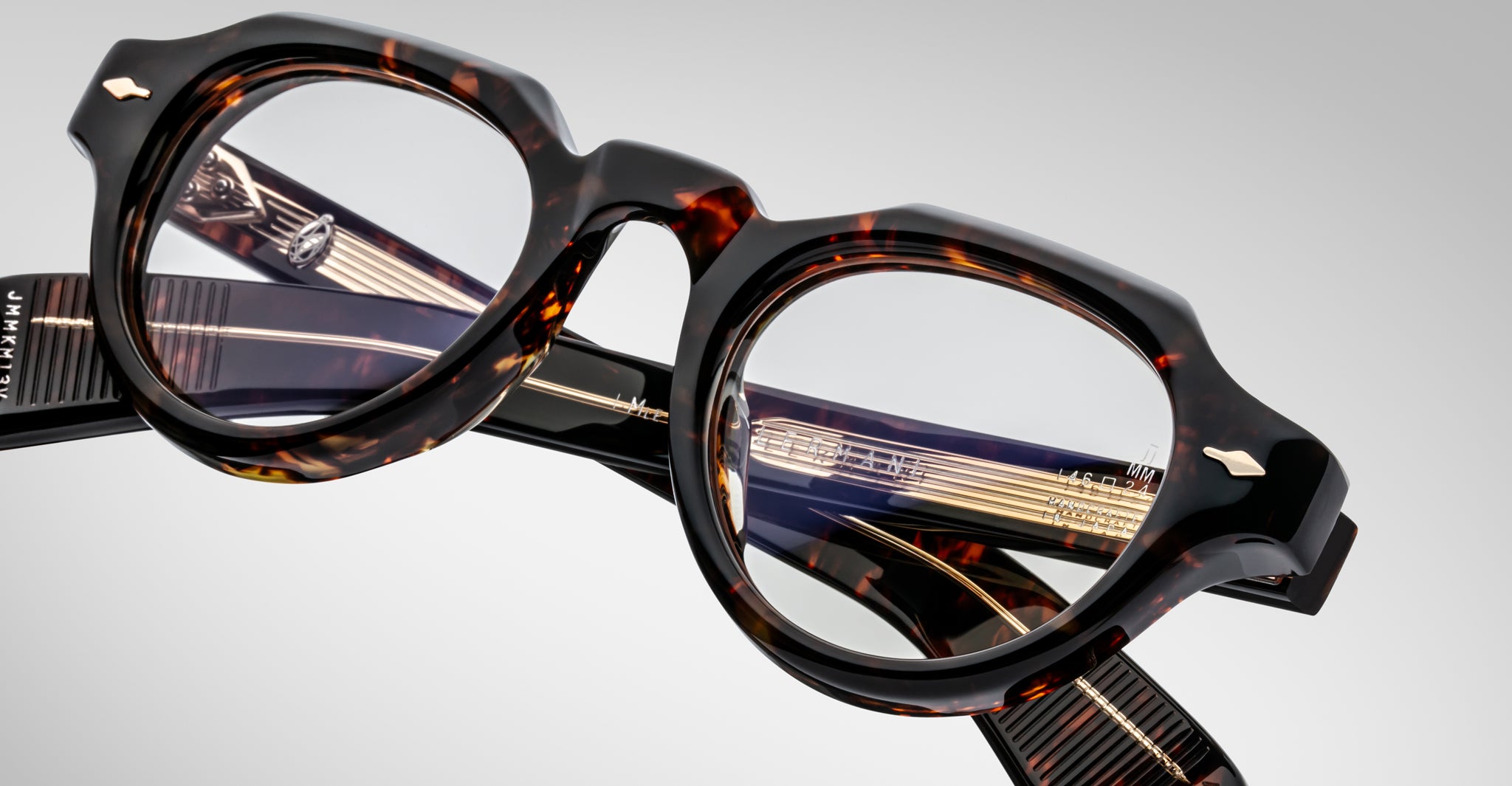 Close-up of Jacques Marie Mage Kellerman eyeglasses featuring round lenses and gold-detailed arms, displayed at an angle on a neutral background. Both the frame’s tortoiseshell design and lens details are clearly visible.