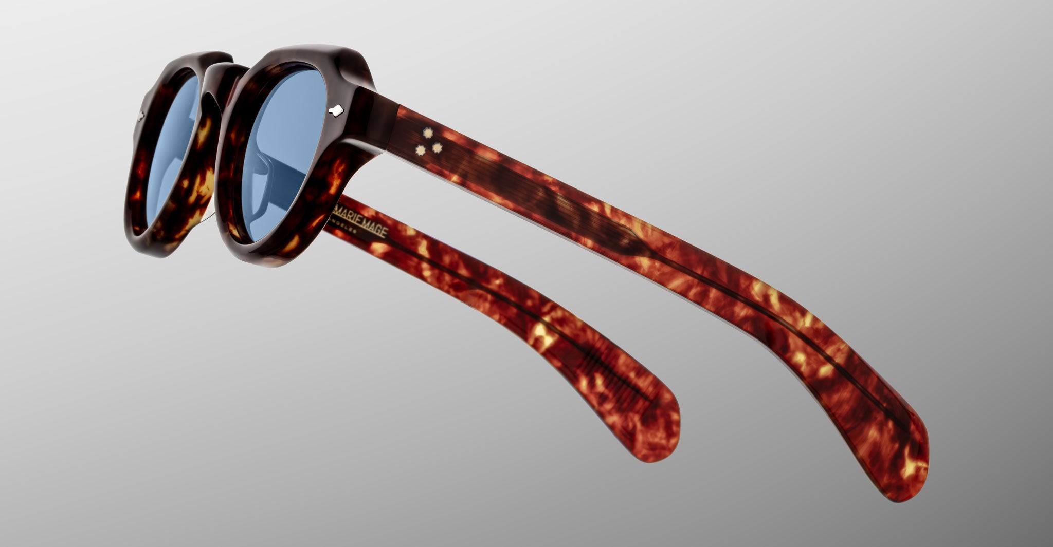 A pair of Jacques Marie Mage Kellerman tortoiseshell sunglasses with round blue lenses, shown at a three-quarter angle on a plain light gray background. The arms of the sunglasses are extended.
