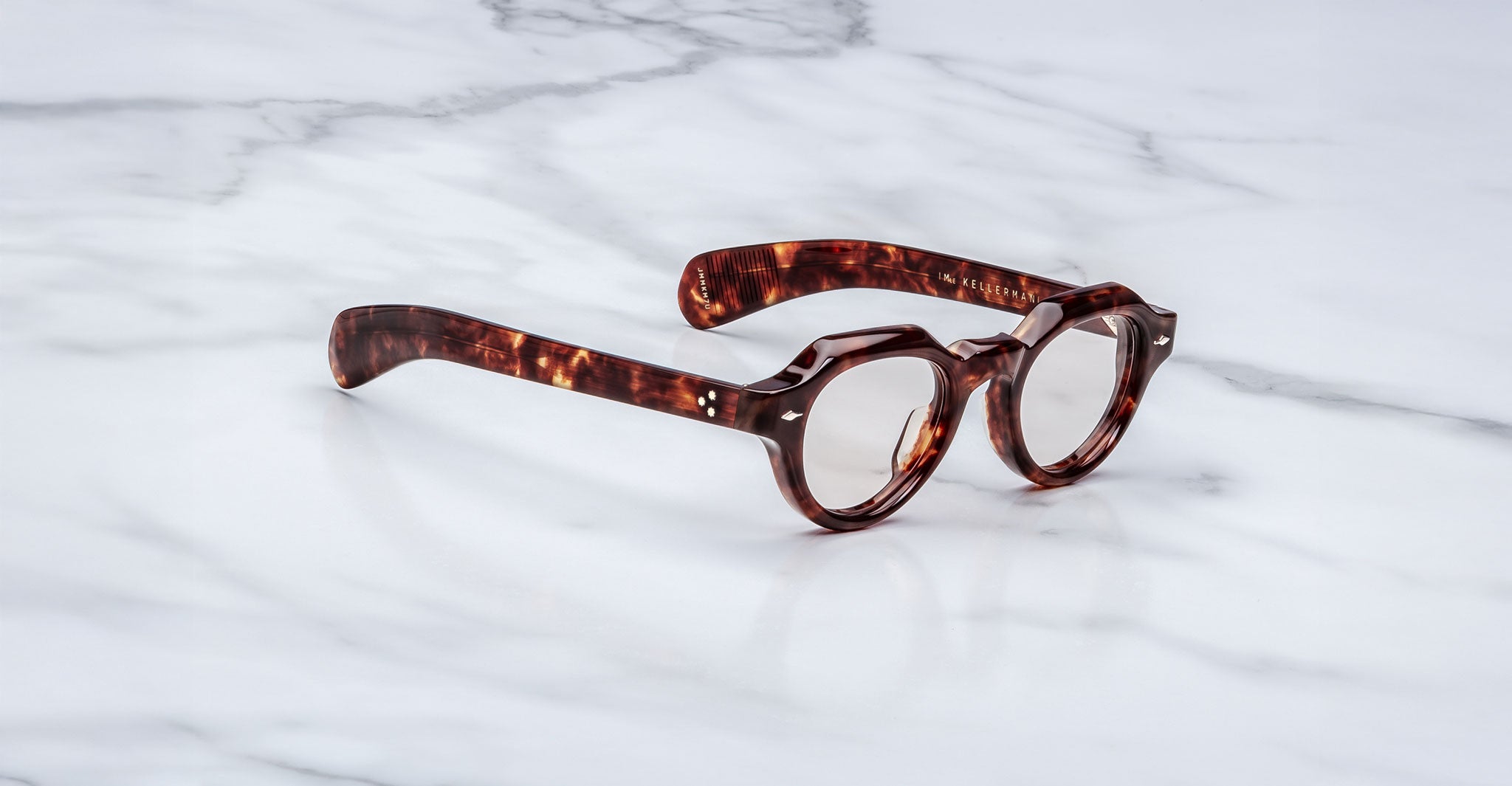 A pair of Jacques Marie Mage Kellerman round, thick-framed tortoiseshell eyeglasses rests on a white marble surface.