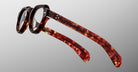 The Jacques Marie Mage Kellerman features round lenses and thick tortoiseshell frames, shown at an angle to highlight the distinctive arms and side details against a plain grey background.