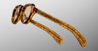 The Jacques Marie Mage Kellerman eyeglasses feature round lenses and thick tortoiseshell frames with patterned arms, displayed from a side angle against a plain gray background.