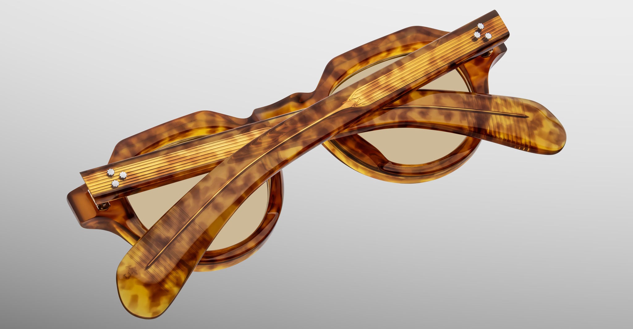 A pair of Jacques Marie Mage Kellerman sunglasses in a tortoiseshell pattern is displayed folded, with the arms crossed over the lenses, set against a soft gradient background.
