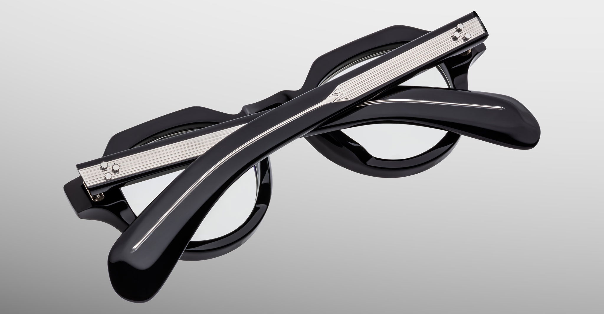 The Jacques Marie Mage Kellerman eyeglasses, featuring black round frames with silver accents, are shown folded with crossed temples on a plain gray background.