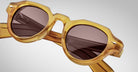 Close-up of Jacques Marie Mage Kellerman sunglasses featuring thick, translucent yellow frames and dark round lenses. The light, blurred background accentuates the eyewear’s texture and stylish details.