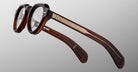 The Jacques Marie Mage Kellerman eyeglasses feature thick brown tortoiseshell frames with metal-accented arms, shown from a side and slightly overhead angle against a plain light gray background.