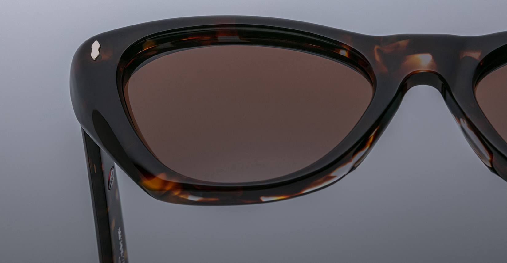 Close-up of the Jacques Marie Mage Kelly sunglasses in tortoiseshell, featuring dark brown lenses and highlighting the upper half of the frame against a plain gray background.