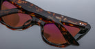 Close-up of two pairs of Jacques Marie Mage Kelly tortoiseshell sunglasses with dark reddish lenses, stacked on a reflective surface to highlight their distinctive frames and lens colors.