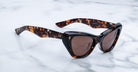 The Jacques Marie Mage Kelly sunglasses, featuring a tortoiseshell pattern and brown lenses, rest on a white marble surface.