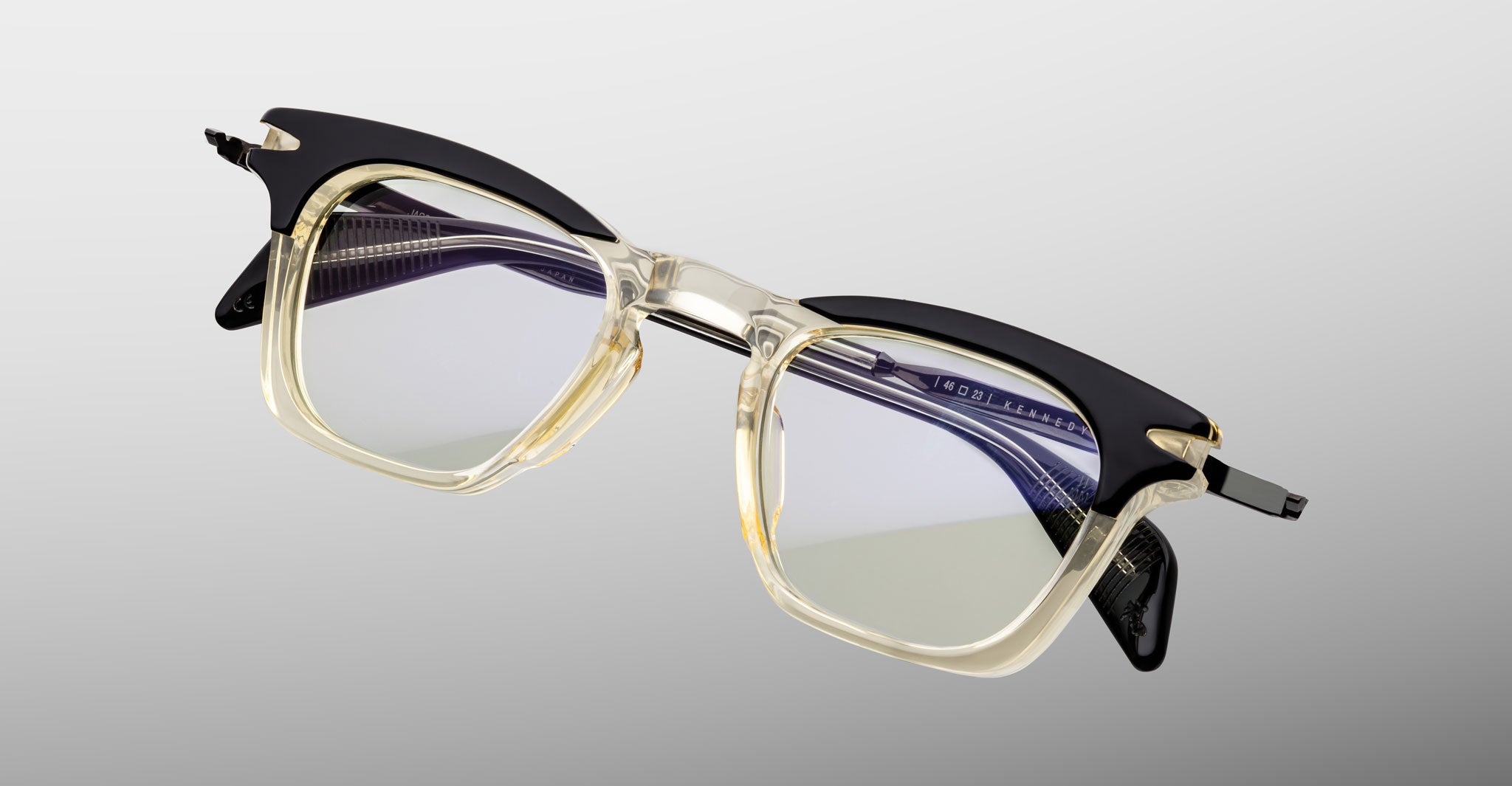 Jacques Marie Mage Kennedy eyeglasses, rectangular shape, clear and black translucent frames with reflective lenses, front view.
