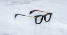 Jacques Marie Mage Kennedy rectangular eyeglasses in black and gold, tortoiseshell temples, front view.