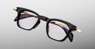Jacques Marie Mage Kennedy black rectangular eyeglasses with gold temple accents, front angle view.