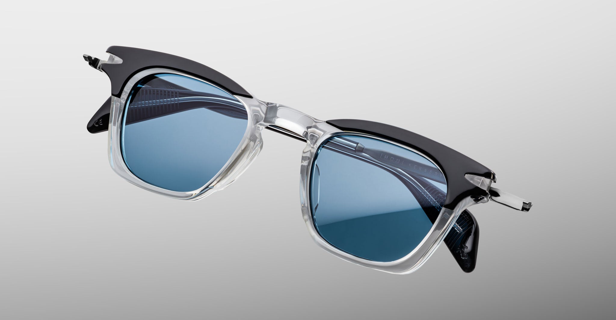 Jacques Marie Mage Kennedy sunglasses with blue-tinted lenses and clear-black frames, shown from above.