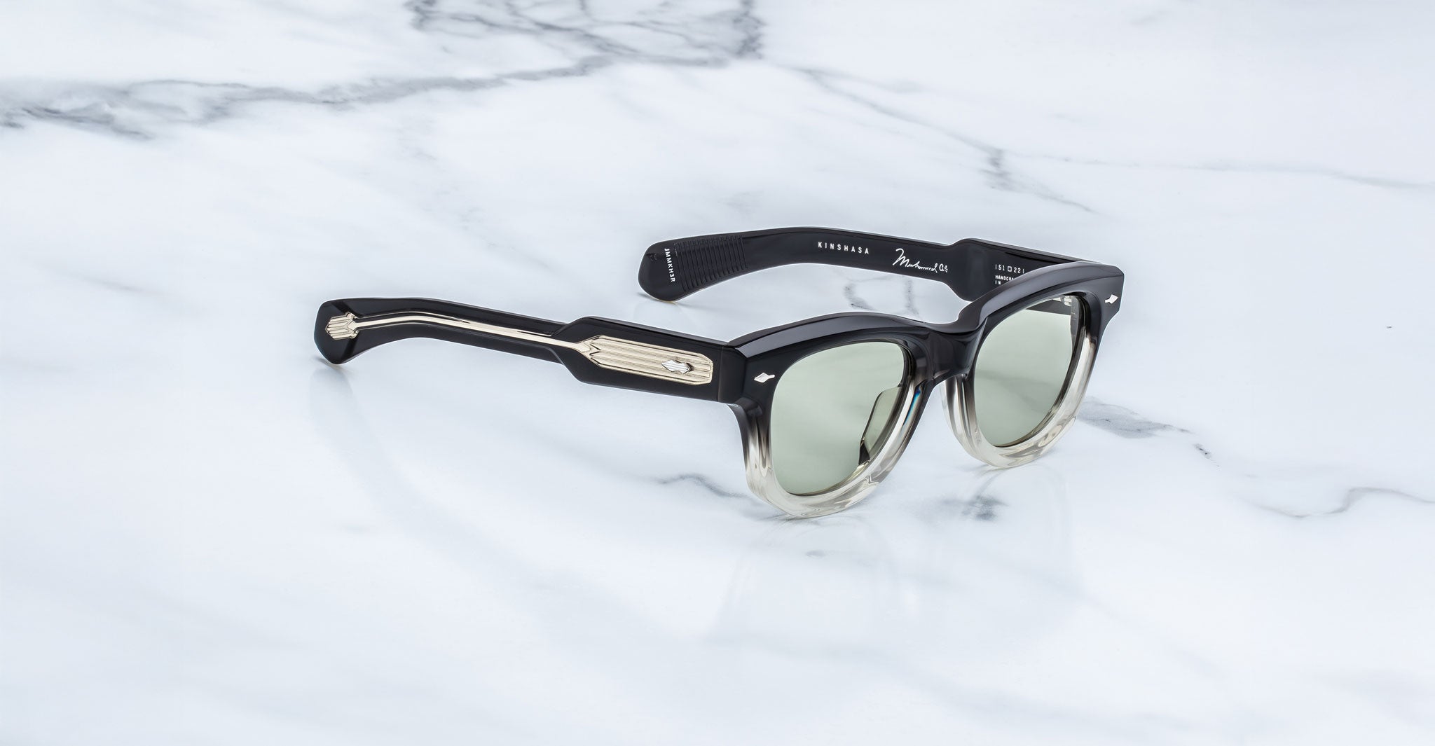 Jacques Marie Mage Kinshasa sunglasses, black and gold frame with green lenses, shown from above.