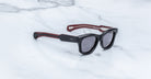 Jacques Marie Mage Kinshasa sunglasses with dark lenses and red-accented arms, viewed from above.