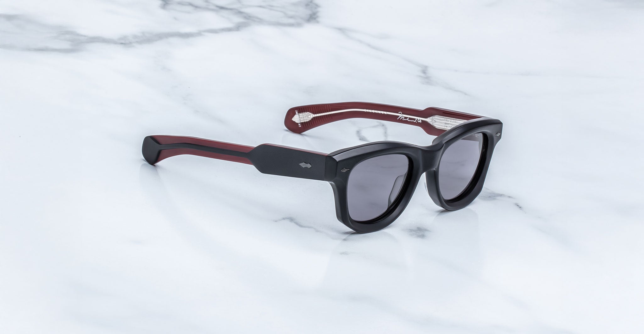 Jacques Marie Mage Kinshasa sunglasses with dark lenses and red-accented arms, viewed from above.