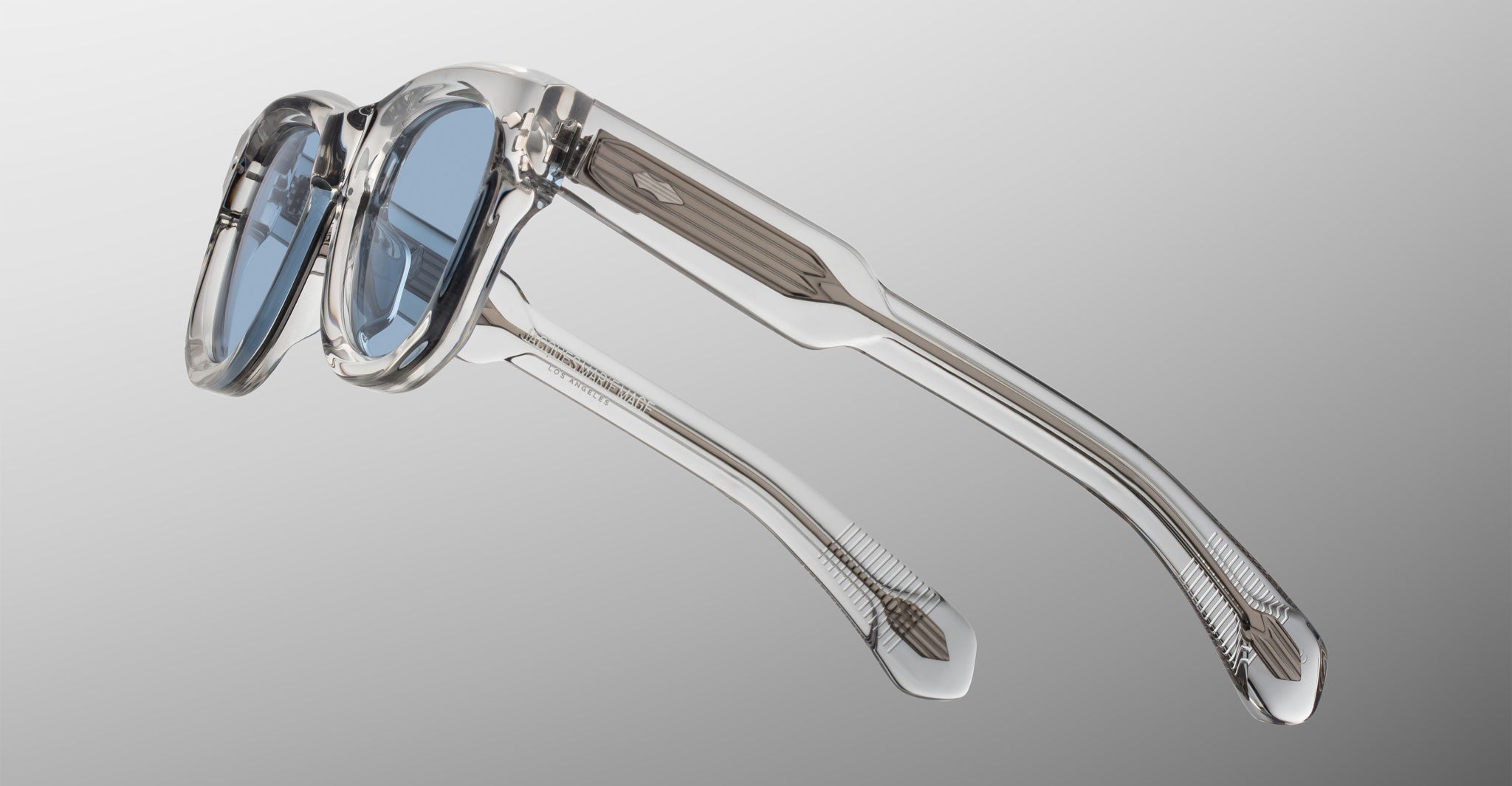 Jacques Marie Mage Kinshasa sunglasses, clear frames, blue lenses, shown at an angle.