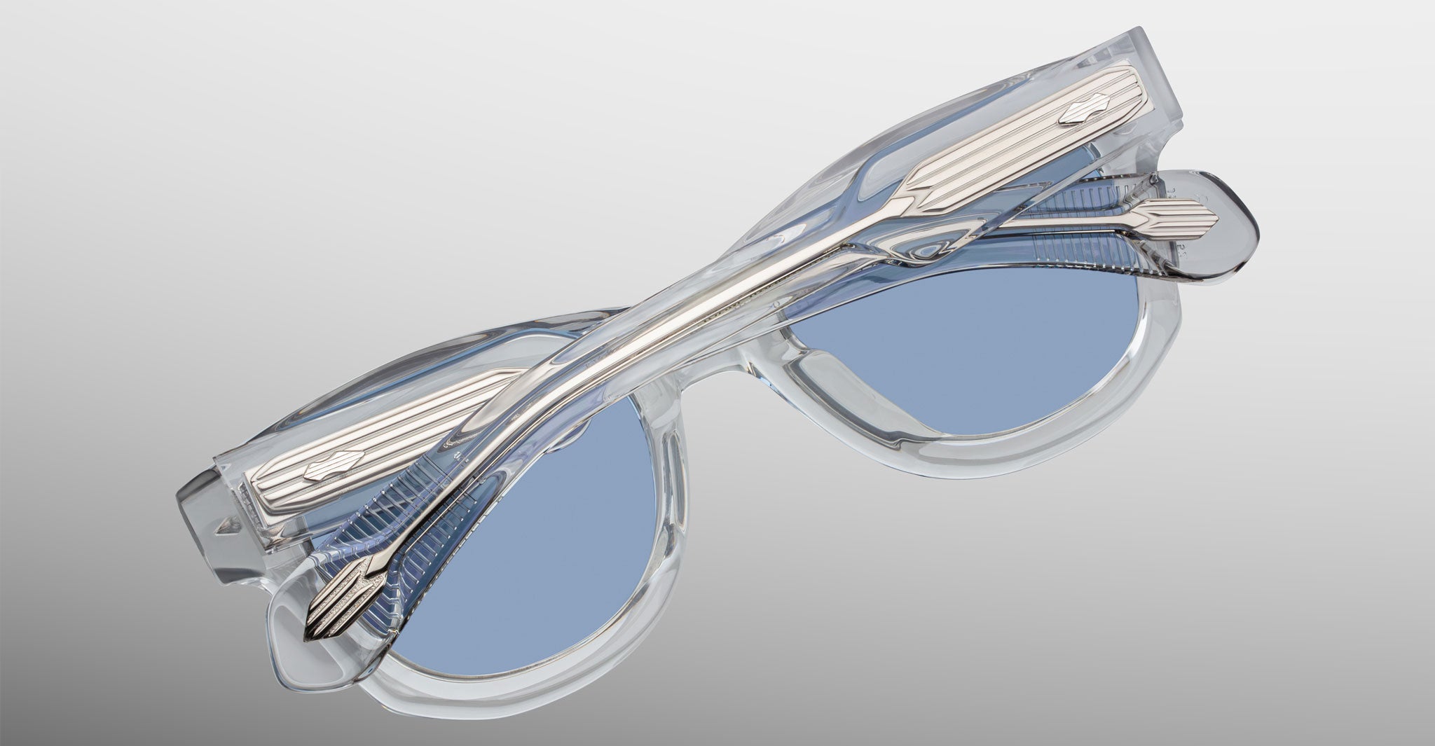 Jacques Marie Mage Kinshasa sunglasses with clear frames, blue-tinted lenses, metallic temples; top-down view.
