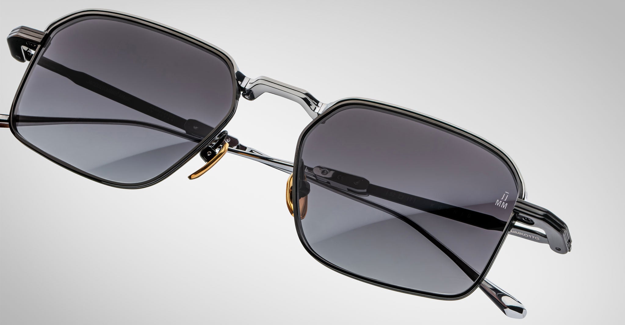 A close-up of Jacques Marie Mage Koenig sunglasses featuring modern rectangular dark lenses, thin metal frames, and adjustable nose pads, set on a plain light gray background.