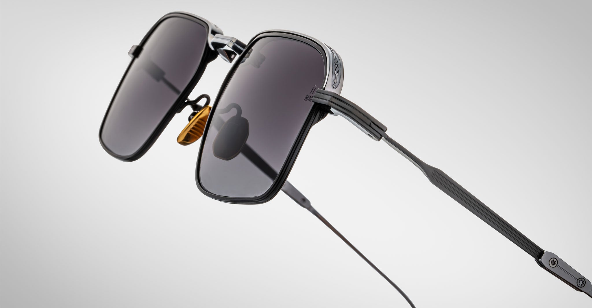 The Jacques Marie Mage Koenig sunglasses feature a black rectangular design with dark tinted lenses, thin metal frame, adjustable nose pads, and straight temples, shown against a plain light background.