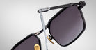 Close-up of Jacques Marie Mage Koenig black square sunglasses with gold nose pads and metallic arms, highlighting hinge details against a plain light background.