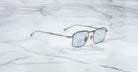 Jacques Marie Mage Koenig silver metal-framed square sunglasses with light-tinted lenses rest on a white marble surface.