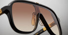 Close-up of Jacques Marie Mage Kurokawa sunglasses featuring dark frames, gold accents, and brown gradient lenses, highlighting the detailed texture and reflective surface.