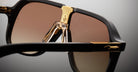 Close-up of Jacques Marie Mage Kurokawa sunglasses featuring brown lenses, black frames, and gold detailing on the bridge and temples, set against a neutral background.