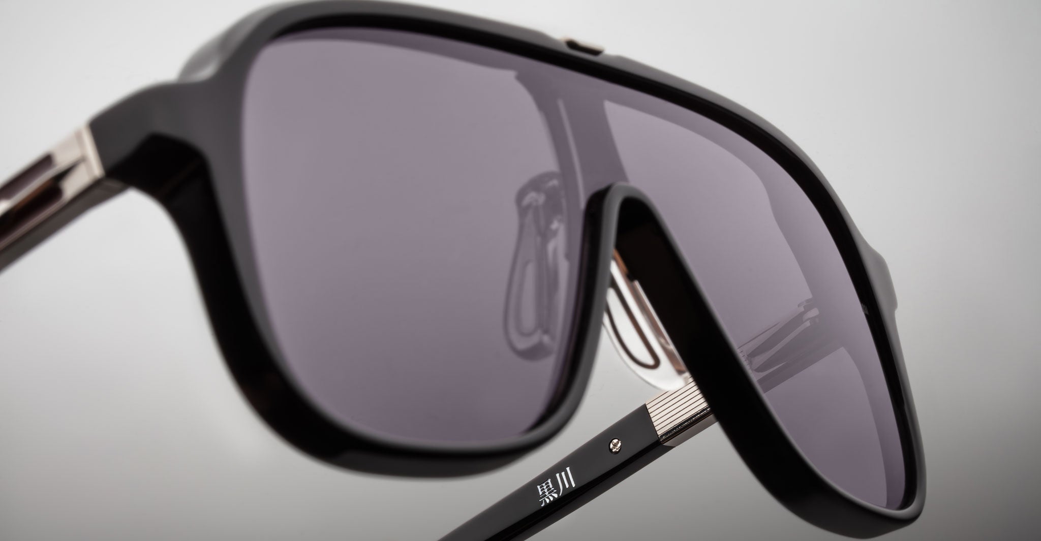 Close-up of Jacques Marie Mage Kurokawa black sunglasses with large, dark-tinted lenses and metal-accented arms, set against a plain, light background.
