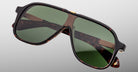 The Jacques Marie Mage Kurokawa is a pair of oversized, tortoiseshell sunglasses with green-tinted lenses and gold accents, displayed on a flat, light gray surface.