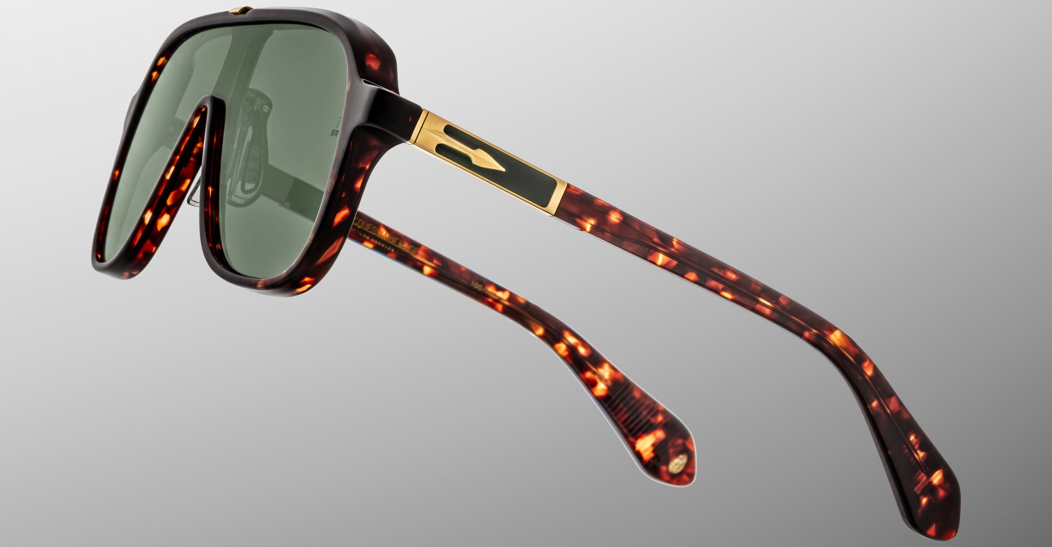 The Jacques Marie Mage Kurokawa sunglasses feature large green-tinted lenses, tortoiseshell frames with gold accents on the arms, and a modern design, shown against a plain gray background.