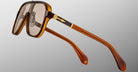 The Jacques Marie Mage Kurokawa sunglasses feature an oversized design with a translucent amber frame, gold accents on the arms, and square-shaped tinted lenses, displayed against a plain light gray background.