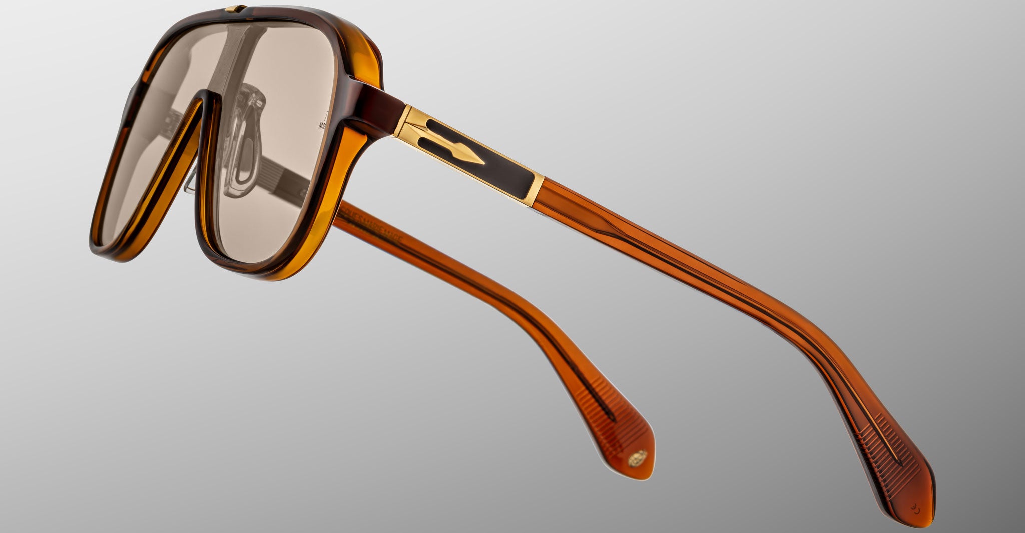 The Jacques Marie Mage Kurokawa sunglasses feature an oversized design with a translucent amber frame, gold accents on the arms, and square-shaped tinted lenses, displayed against a plain light gray background.