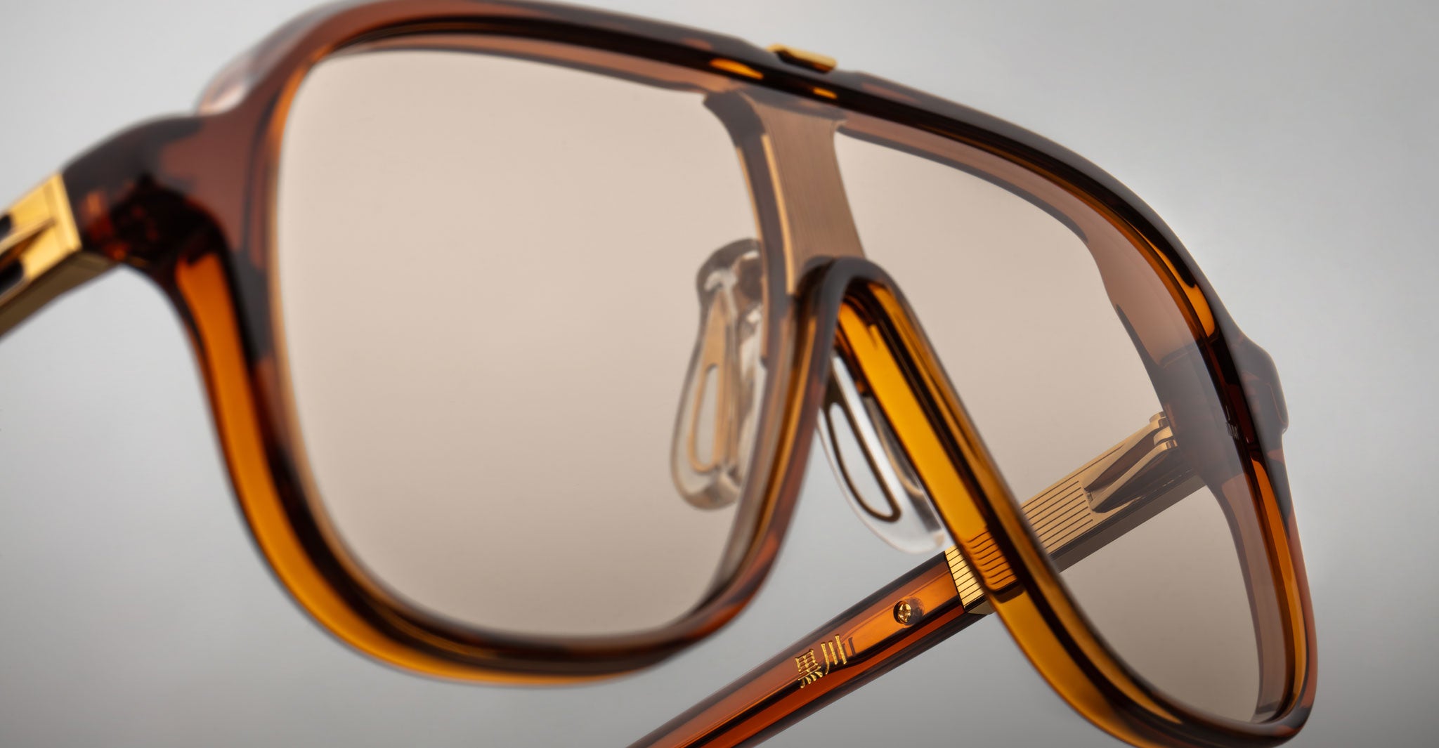 Close-up of Jacques Marie Mage Kurokawa oversized sunglasses featuring brown-tinted lenses and thick amber frames, highlighting nose pads and frame construction against a plain background.