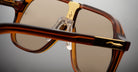Close-up of Jacques Marie Mage Kurokawa sunglasses in brown and gold, featuring clear nose pads, a detailed gold bridge, and frame accents set against a neutral background.