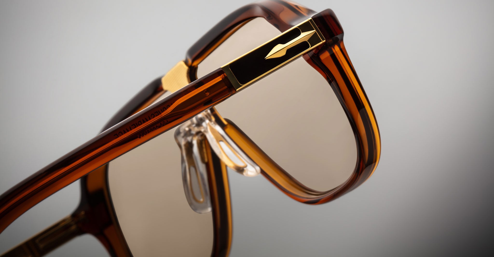 Close-up of Jacques Marie Mage Kurokawa eyeglasses in brown and gold, highlighting transparent nose pads, hinge, and frame details against a neutral background.