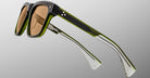 The Jacques Marie Mage Lankaster sunglasses feature thick, square black and green frames, brown-tinted lenses, transparent arm tips, and the brand name visible on the inner side of the arm.