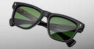 The Jacques Marie Mage Lankaster sunglasses feature a black rectangular frame with green-tinted lenses, gold accents at the front corners, and visible gold detailing on the inner arms, displayed on a light gray background.