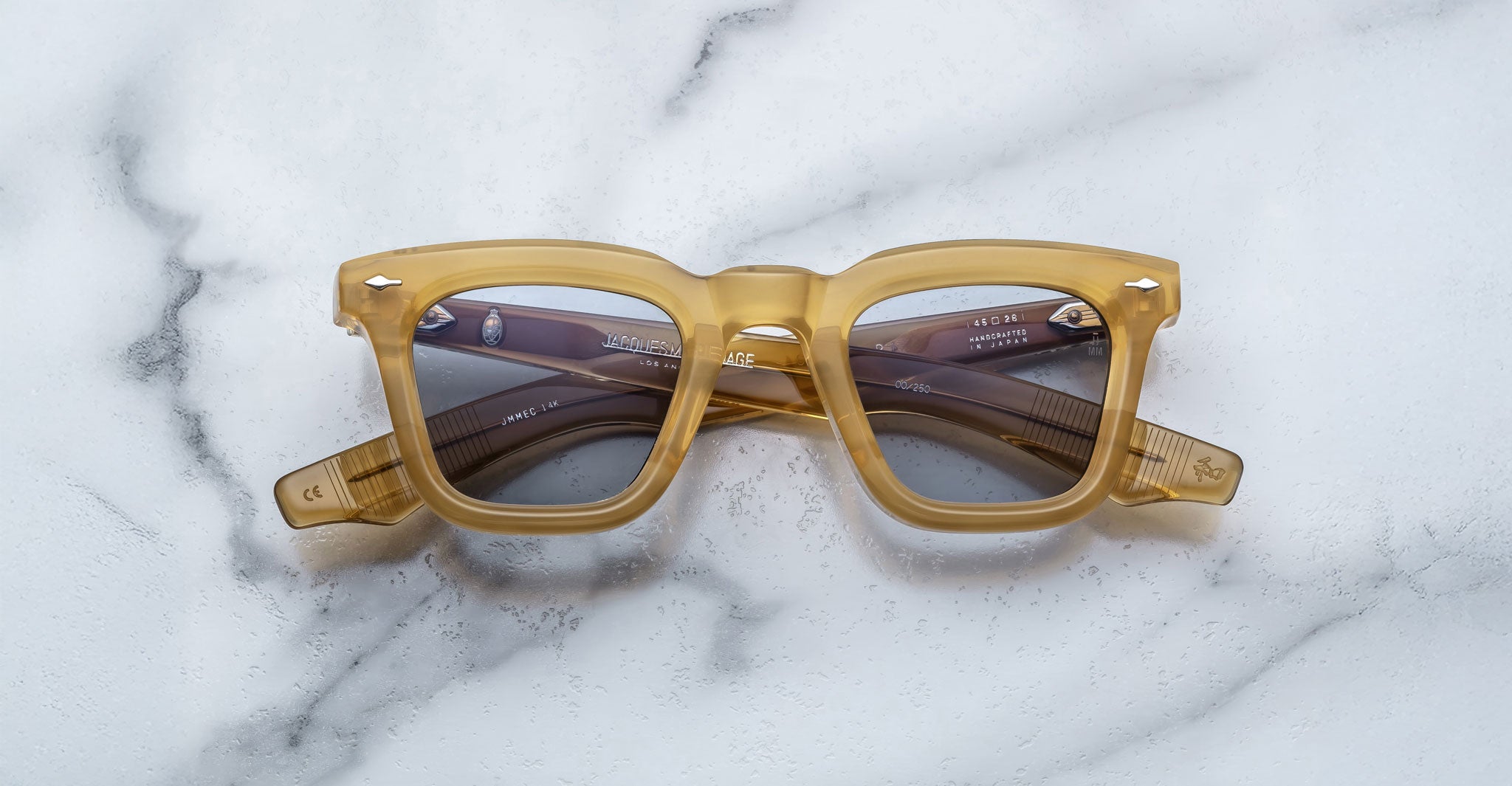 Jacques Marie Mage Leclair eyeglasses with yellow translucent thick frames and gray tinted lenses rest on a white marble surface, viewed from above.